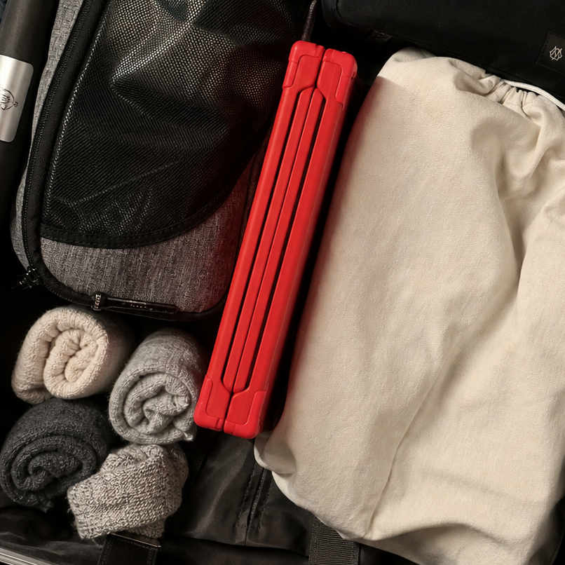 An open silver suitcase packed with travel items, including a black zippered pouch, a beige drawstring bag, and SUNSAL travel collapsible yoga block packed.