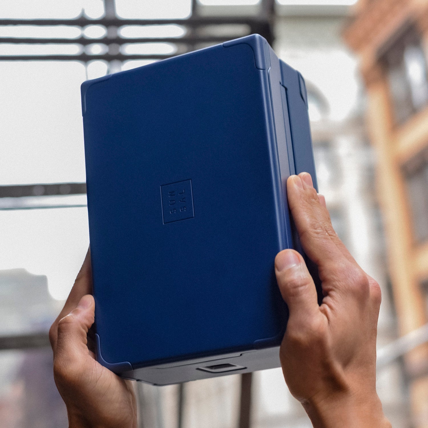 Hands holding a Sunsal yoga block in Navy, showcasing its sleek design against an urban backdrop