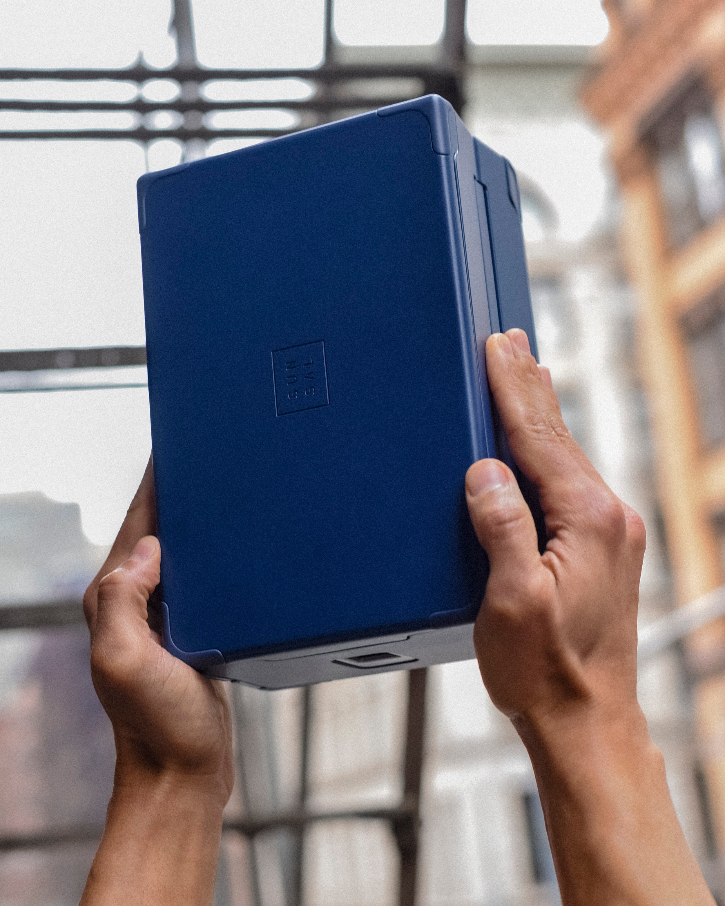Hands holding a Sunsal yoga block in Navy, showcasing its sleek design against an urban backdrop